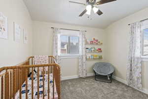 Carpeted bedroom featuring a crib and ceiling fan