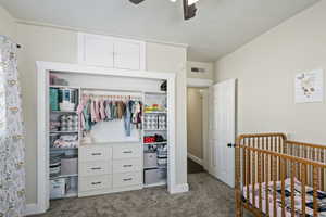 Bedroom featuring a nursery area, ceiling fan, and carpet floors