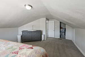 Bedroom featuring vaulted ceiling, dark carpet, and a textured ceiling