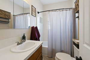 Full bathroom with vanity, shower / bathtub combination with curtain, and toilet