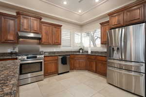 Kitchen with dark stone countertops, light tile patterned floors, sink, and appliances with stainless steel finishes