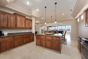 Kitchen with stainless steel stove, a kitchen island, a tray ceiling, light tile patterned flooring, and decorative light fixtures