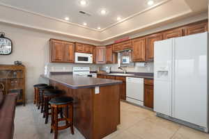 Kitchen with light tile patterned flooring, a breakfast bar, sink, a tray ceiling, and white appliances