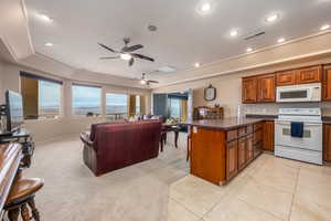 Kitchen with a breakfast bar area, light colored carpet, a raised ceiling, kitchen peninsula, and white appliances