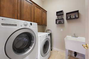 Laundry room featuring cabinets, light tile patterned floors, and washer and clothes dryer