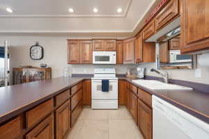 Kitchen featuring white appliances, a tray ceiling, sink, and light tile patterned floors