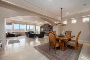 Dining space featuring a stone fireplace, light tile patterned floors, a chandelier, and a tray ceiling