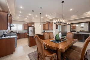 Dining area with crown molding, a tray ceiling, a chandelier, and light tile patterned flooring