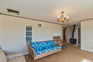 Living room featuring crown molding, a notable chandelier, light carpet, and a wood stove