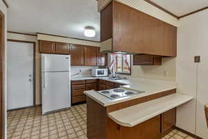 Kitchen featuring a breakfast bar, ornamental molding, white appliances, kitchen peninsula, and a textured ceiling