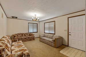 Living room with an inviting chandelier, carpet floors, ornamental molding, and a textured ceiling