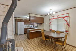 Kitchen featuring a wood stove, an inviting chandelier, white appliances, and kitchen peninsula