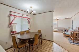 Carpeted dining space with an inviting chandelier, crown molding, and a textured ceiling