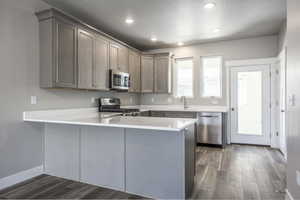 Kitchen featuring dark hardwood / wood-style flooring, sink, kitchen peninsula, and appliances with stainless steel finishes