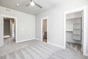 Unfurnished bedroom with ceiling fan, connected bathroom, a spacious closet, light colored carpet, and a closet