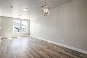 Spare room featuring an inviting chandelier, wood-type flooring, and a textured ceiling