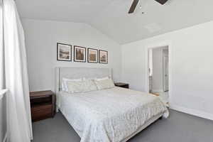 Bedroom featuring ceiling fan, carpet floors, vaulted ceiling, and ensuite bath