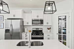 Kitchen featuring white cabinetry, appliances with stainless steel finishes, sink, and decorative light fixtures