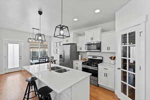 Kitchen with stainless steel appliances, an island with sink, white cabinets, and a kitchen bar