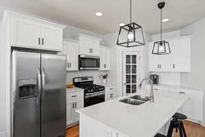 Kitchen with white cabinetry, stainless steel appliances, decorative light fixtures, and sink