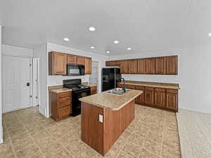 Kitchen featuring sink, a center island with sink, a textured ceiling, and black appliances