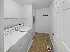 Laundry room featuring dark tile patterned flooring, a textured ceiling, washer and clothes dryer, and electric panel