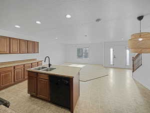 Kitchen featuring sink, hanging light fixtures, a center island with sink, a textured ceiling, and dishwasher