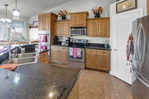 Kitchen featuring lofted ceiling, sink, appliances with stainless steel finishes, an inviting chandelier, and hanging light fixtures