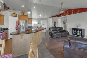 Kitchen with vaulted ceiling, dark hardwood / wood-style floors, an island with sink, stainless steel fridge, and hanging light fixtures