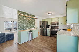 Kitchen featuring sink, light hardwood / wood-style flooring, green cabinets, stainless steel appliances, and tasteful backsplash