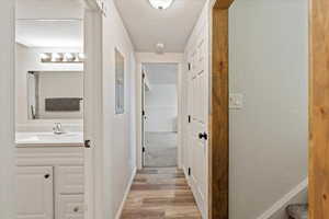 Hallway featuring light wood-type flooring, sink, and a textured ceiling