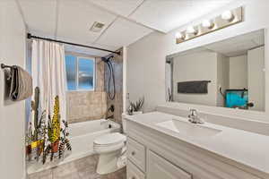 Full bathroom featuring tile patterned flooring, vanity, shower / bath combination with curtain, a drop ceiling, and toilet