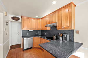 Kitchen featuring sink, black electric stovetop, light hardwood / wood-style floors, stainless steel dishwasher, and kitchen peninsula