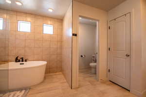 Bathroom with tile walls, a tub to relax in, and toilet