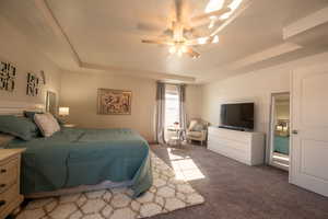 Bedroom featuring dark carpet, a tray ceiling, and ceiling fan