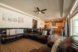 Living room featuring ceiling fan, a tray ceiling, dark wood-type flooring, and a textured ceiling