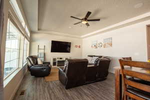 Living room with ceiling fan, a tray ceiling, dark hardwood / wood-style flooring, and a textured ceiling
