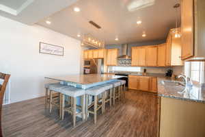 Kitchen featuring wall chimney range hood, sink, appliances with stainless steel finishes, a kitchen island, and dark stone counters