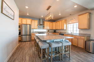 Kitchen with appliances with stainless steel finishes, decorative light fixtures, a center island, light stone counters, and wall chimney range hood