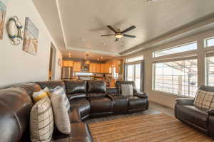 Living room featuring a tray ceiling, a textured ceiling, ceiling fan, and light wood-type flooring