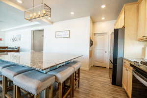 Kitchen featuring pendant lighting, a breakfast bar area, light hardwood / wood-style flooring, stainless steel appliances, and light brown cabinetry