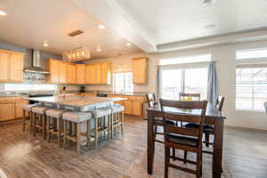 Kitchen with wall chimney range hood, a center island, light stone countertops, dark hardwood / wood-style flooring, and light brown cabinets