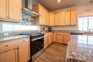 Kitchen featuring light stone countertops, gas stove, hardwood / wood-style floors, and wall chimney range hood