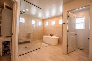 Bathroom with shower with separate bathtub, tile walls, and a textured ceiling
