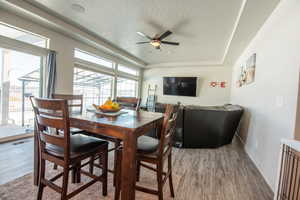 Dining room featuring ceiling fan, hardwood / wood-style floors, a textured ceiling, and a tray ceiling