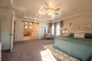 Bedroom featuring ensuite bathroom, carpet flooring, ceiling fan, a tray ceiling, and a barn door