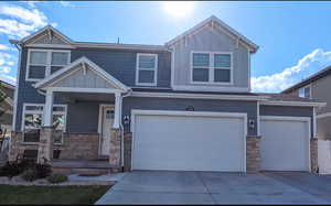 Craftsman-style home with board and batten siding, stone siding, driveway, and an attached garage