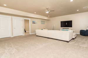 Carpeted living room featuring ceiling fan and a textured ceiling