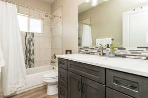 Full bathroom featuring hardwood / wood-style flooring, vanity, tasteful backsplash, shower / bath combination with curtain, and toilet