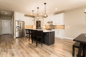 Kitchen with stainless steel appliances, white cabinetry, hanging light fixtures, and a kitchen island with sink